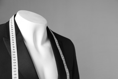 Photo of Male mannequin with black jacket and measuring tape on grey background, closeup. Space for text