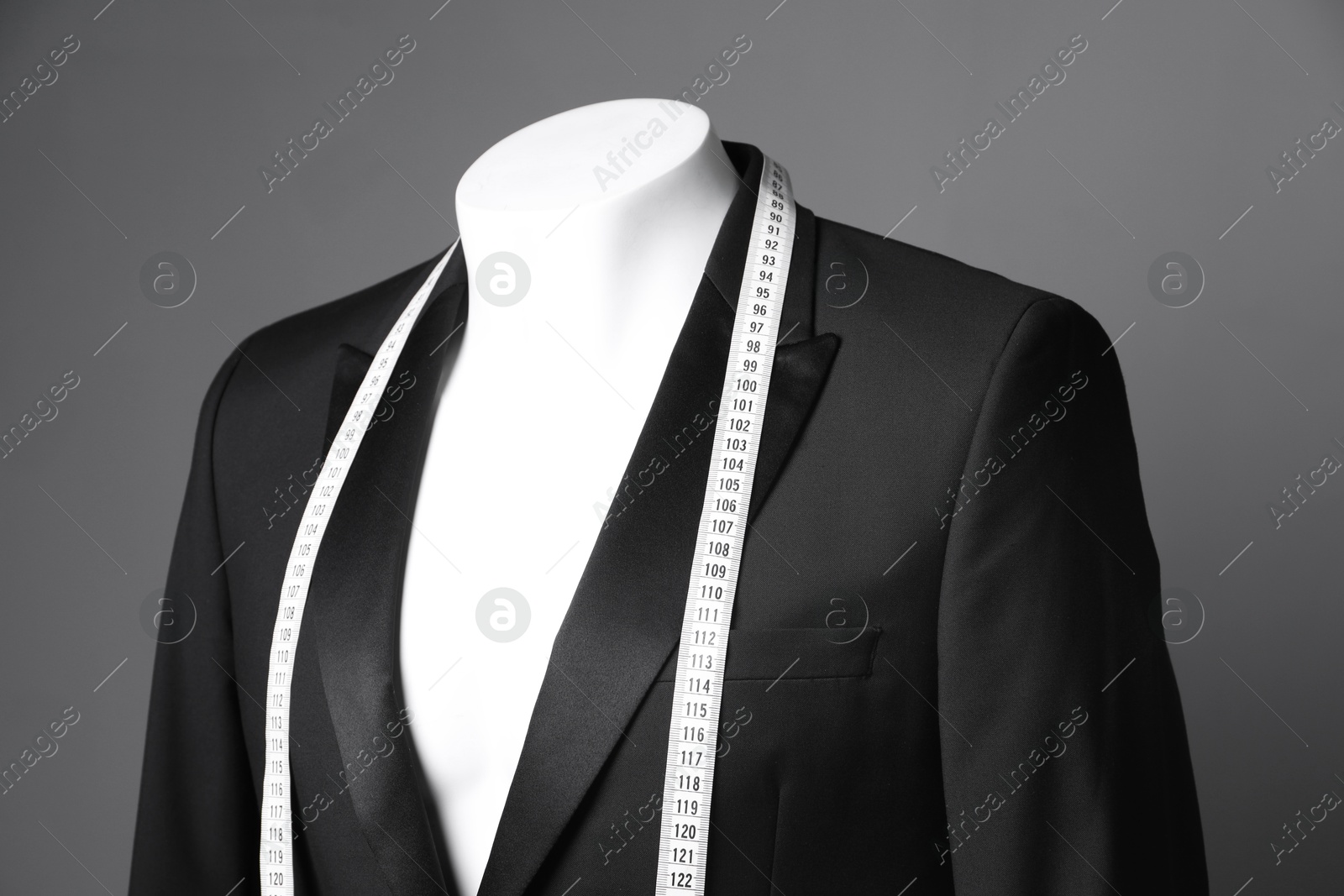 Photo of Male mannequin with black jacket and measuring tape on grey background, closeup