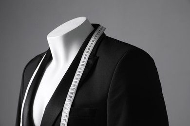 Photo of Male mannequin with black jacket and measuring tape on grey background, closeup