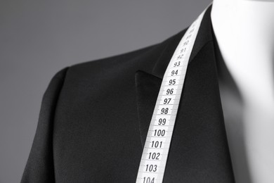 Photo of Mannequin with black jacket and measuring tape on grey background, closeup