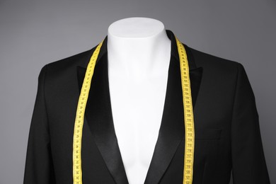 Photo of Male mannequin with black jacket and measuring tape on grey background, closeup