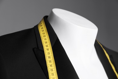 Photo of Mannequin with black jacket and measuring tape on grey background, closeup