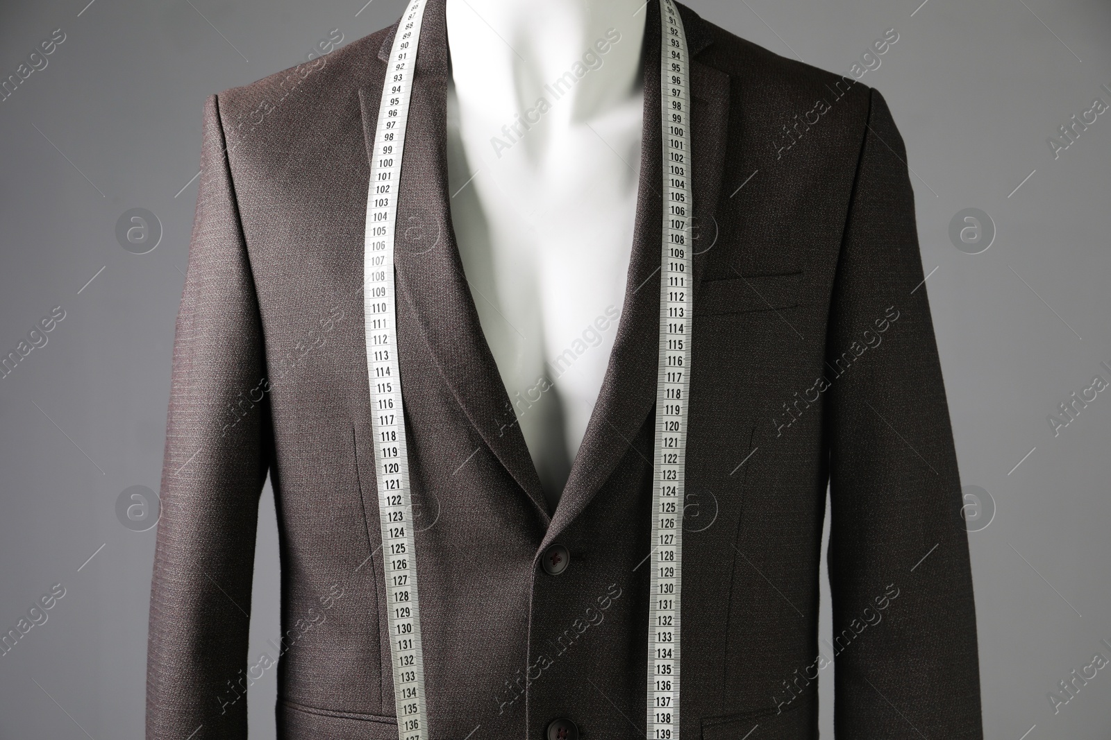 Photo of Male mannequin with brown jacket and measuring tape on grey background, closeup