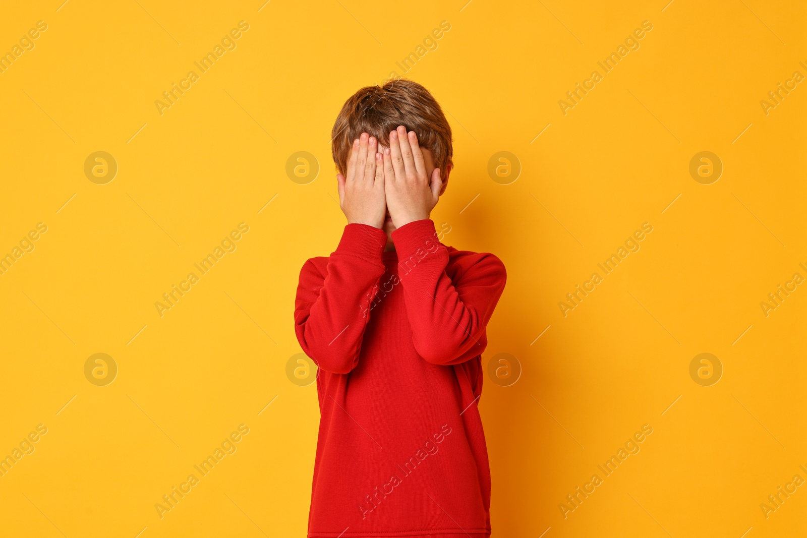 Photo of Scared little boy covering face on orange background