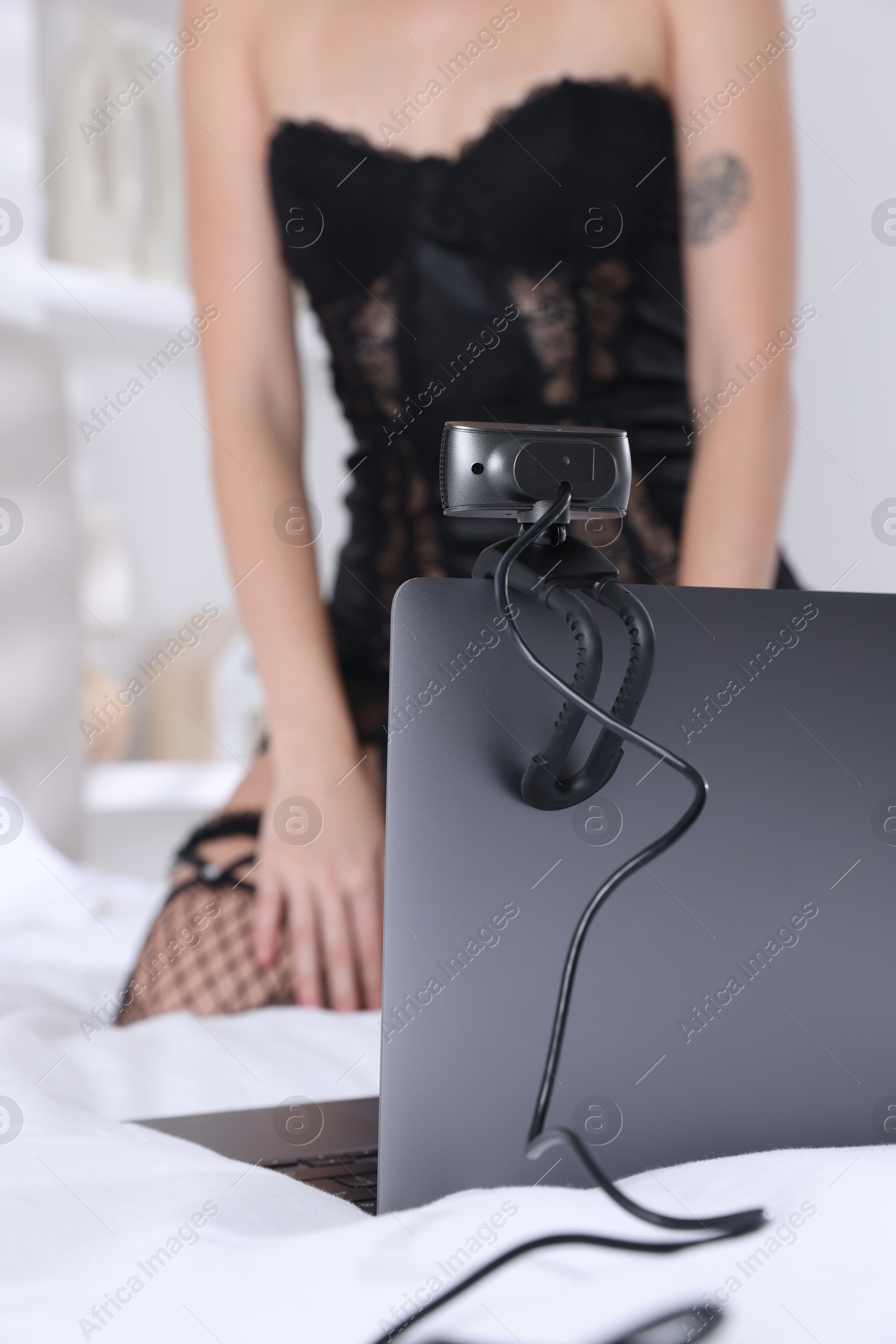 Photo of Prostitution. Webcam model in underwear streaming with laptop on bed, selective focus