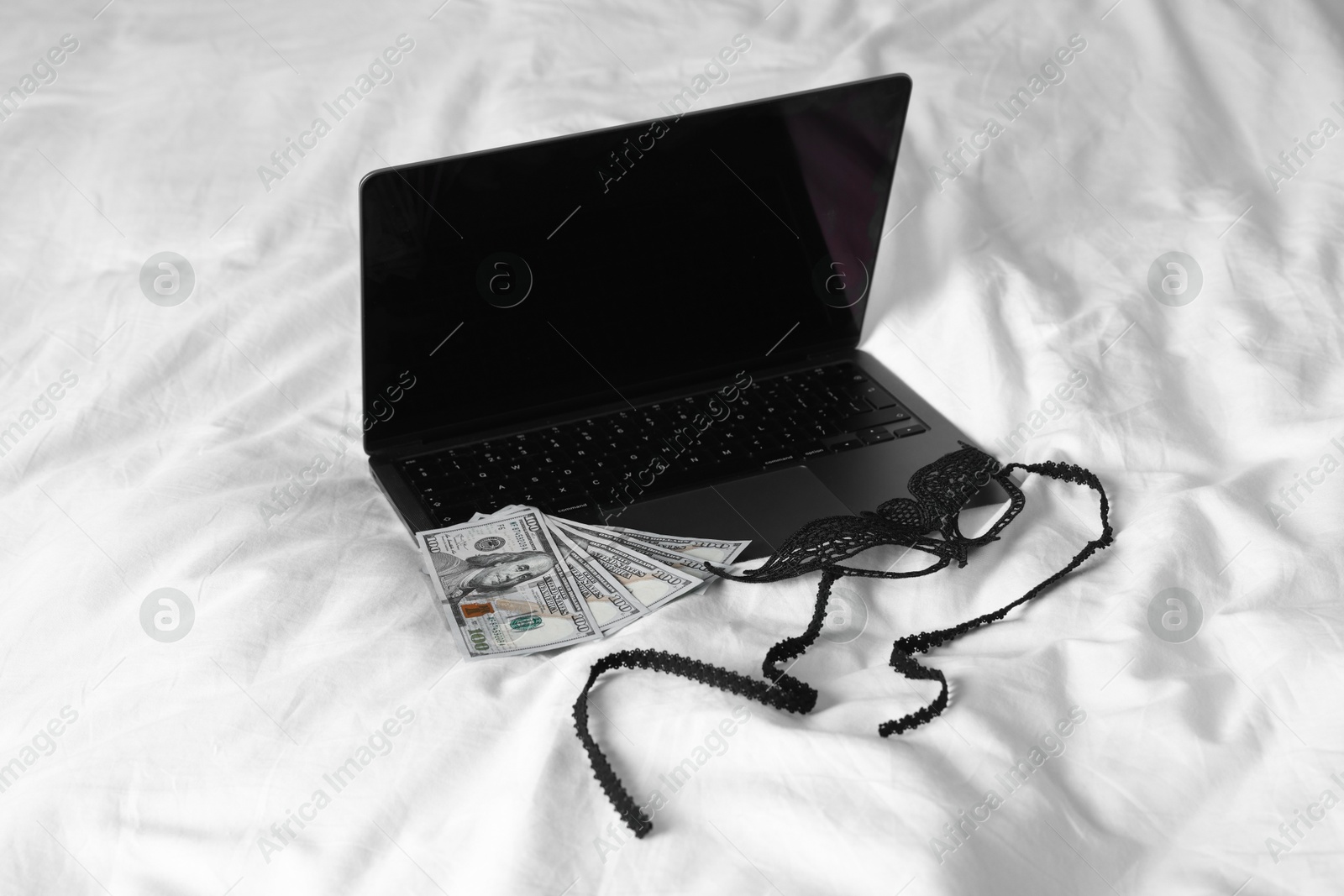 Photo of Prostitution and virtual sex. Laptop, dollar banknotes and mask on linens