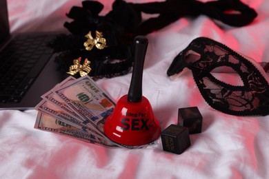 Prostitution and virtual sex. Laptop, dollar banknotes, bell and dices on linens