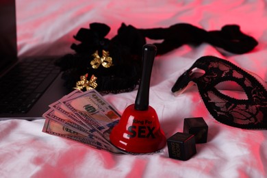 Photo of Prostitution and virtual sex. Laptop, dollar banknotes, bell and dices on linens