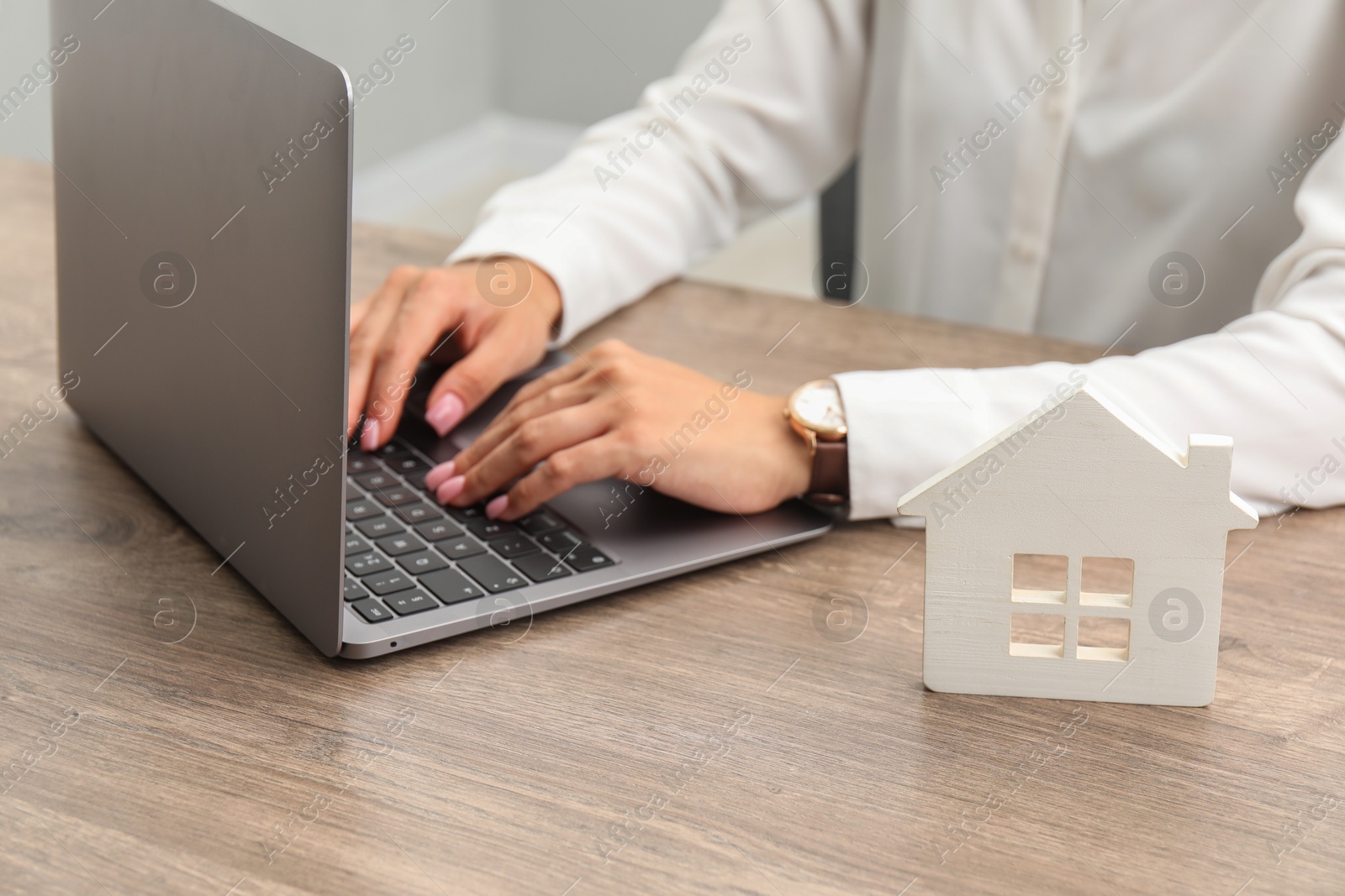 Photo of House hunting. Woman with laptop and house figure at wooden table, closeup