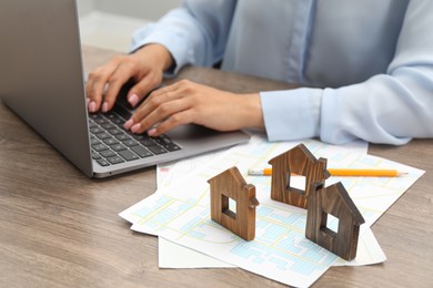 Photo of House hunting. Woman with laptop, papers and house figures at wooden table, closeup