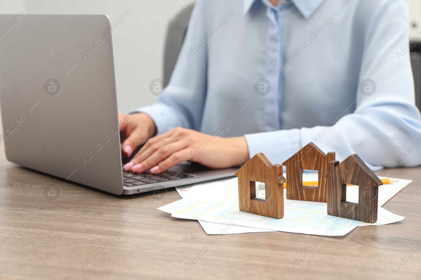 Photo of House hunting. Woman with laptop, papers and house figures at wooden table, closeup