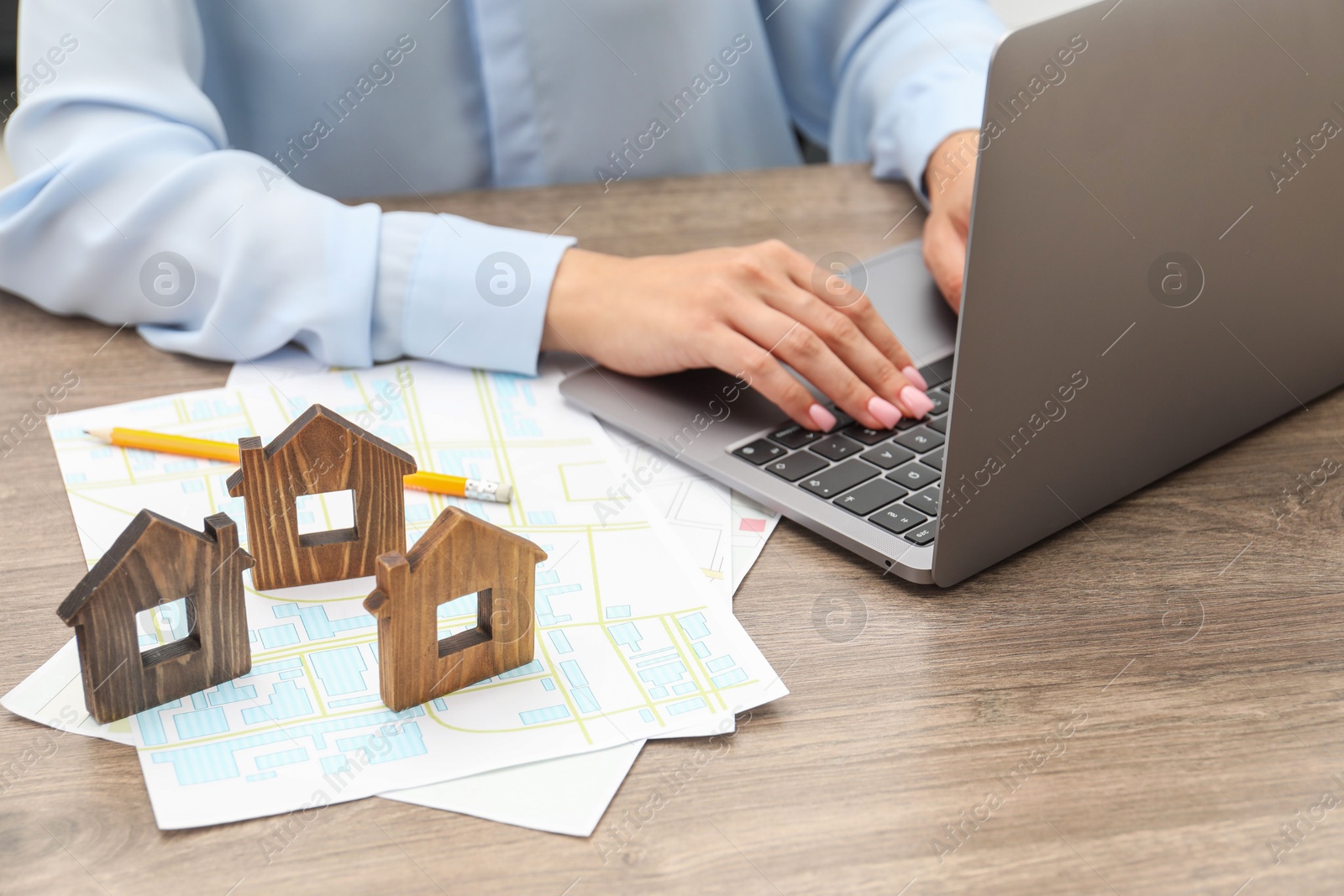 Photo of House hunting. Woman with laptop, papers and house figures at wooden table, closeup