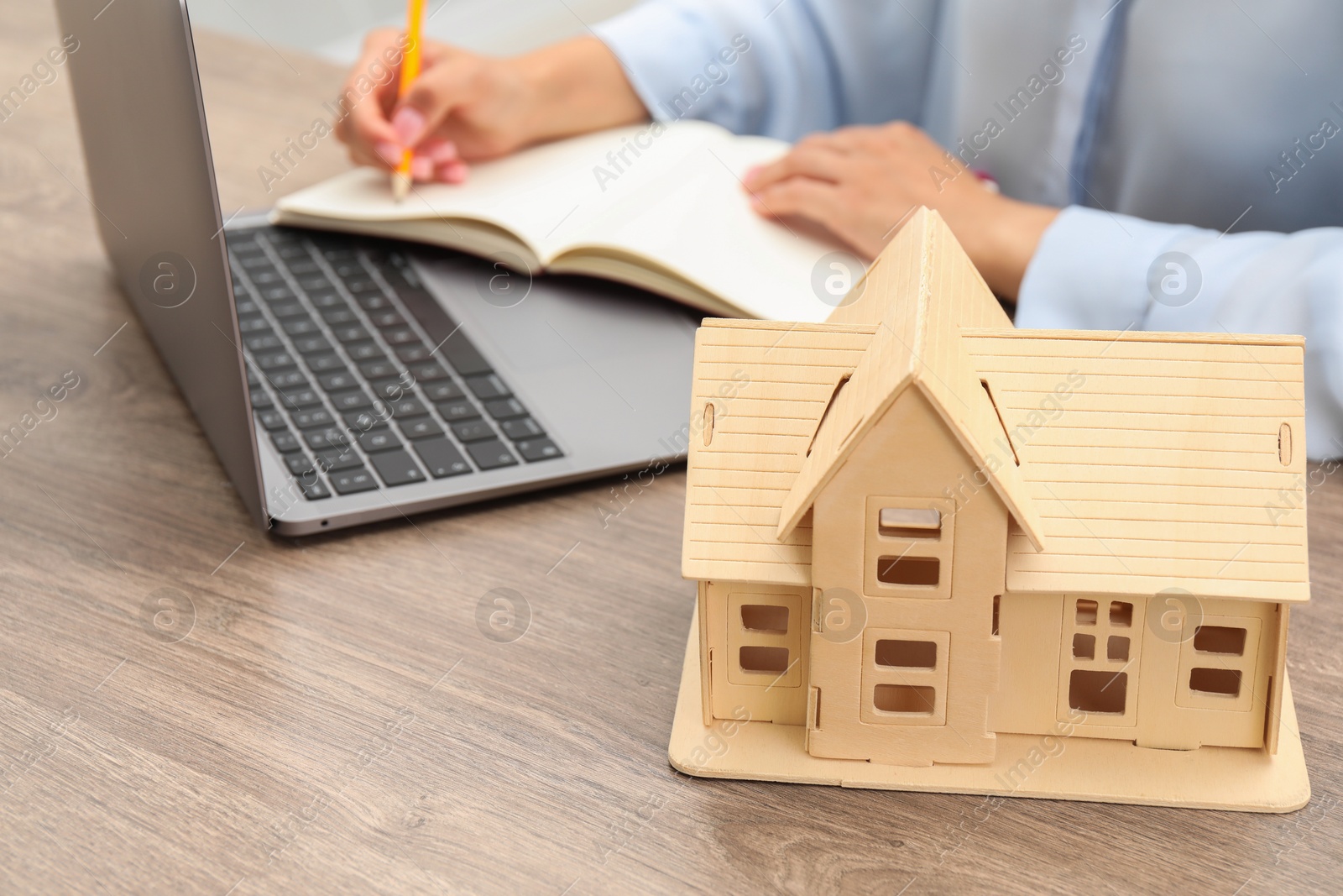 Photo of House hunting. Woman with laptop and house figure at wooden table, closeup