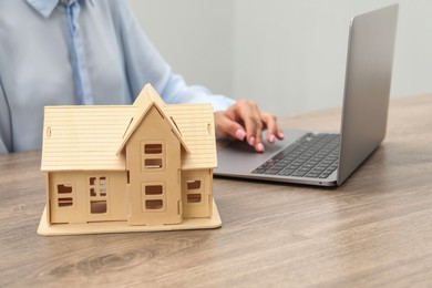 Photo of House hunting. Woman with laptop and house figure at wooden table, closeup