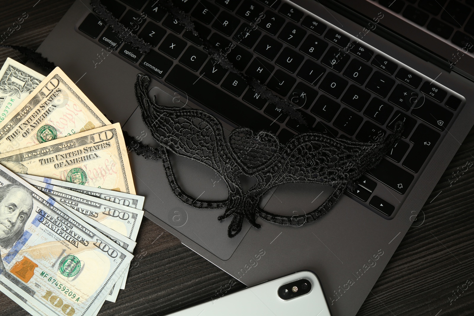 Photo of Sex work. Laptop, mask, smartphone and money on wooden surface, closeup