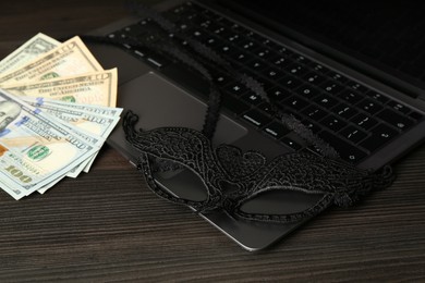 Photo of Sex work. Laptop, mask and money on wooden surface, closeup