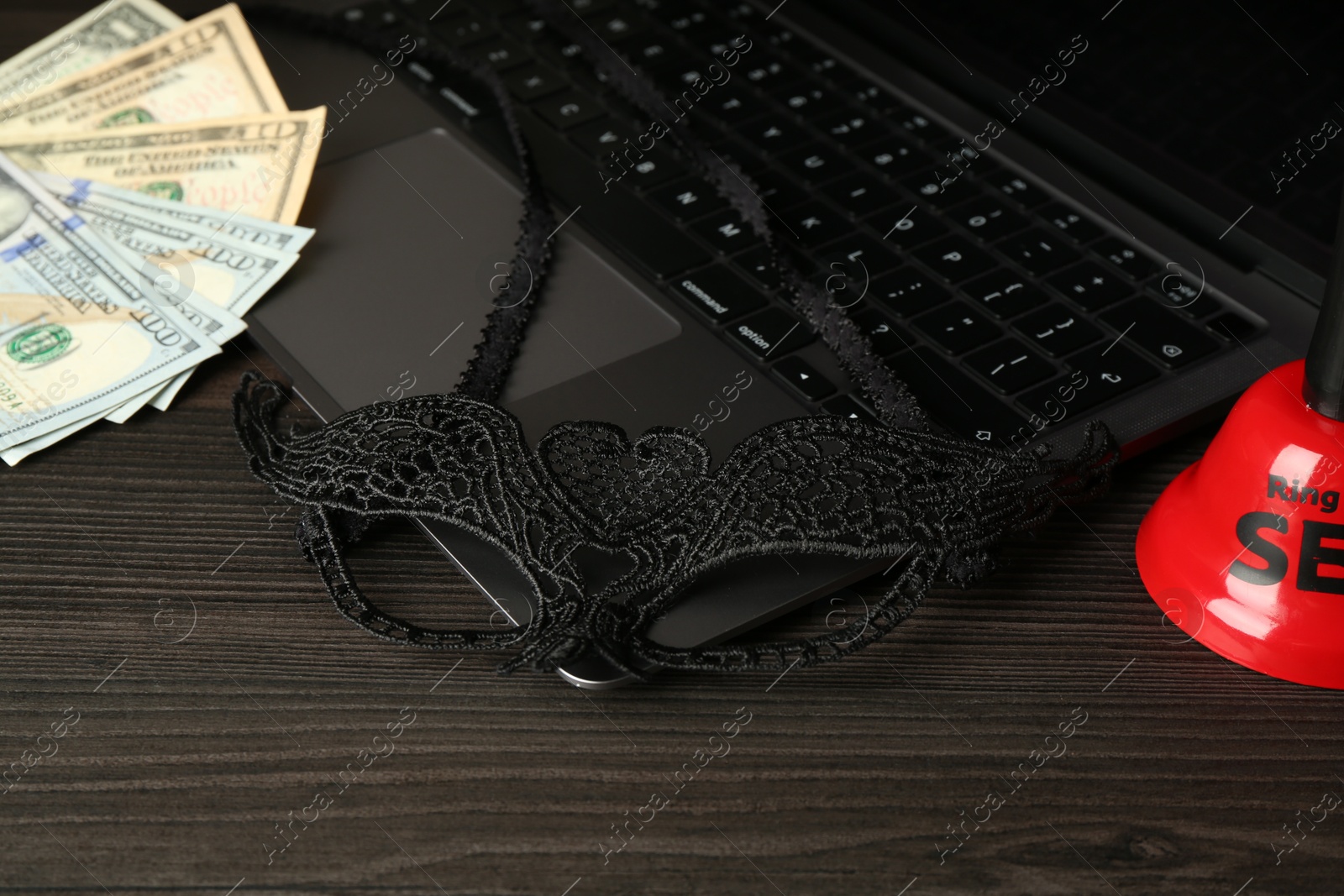 Photo of Sex work. Laptop, mask, money and bell on wooden surface, closeup