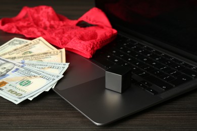 Photo of Sex work. Laptop, lingerie, dice and money on wooden surface, closeup