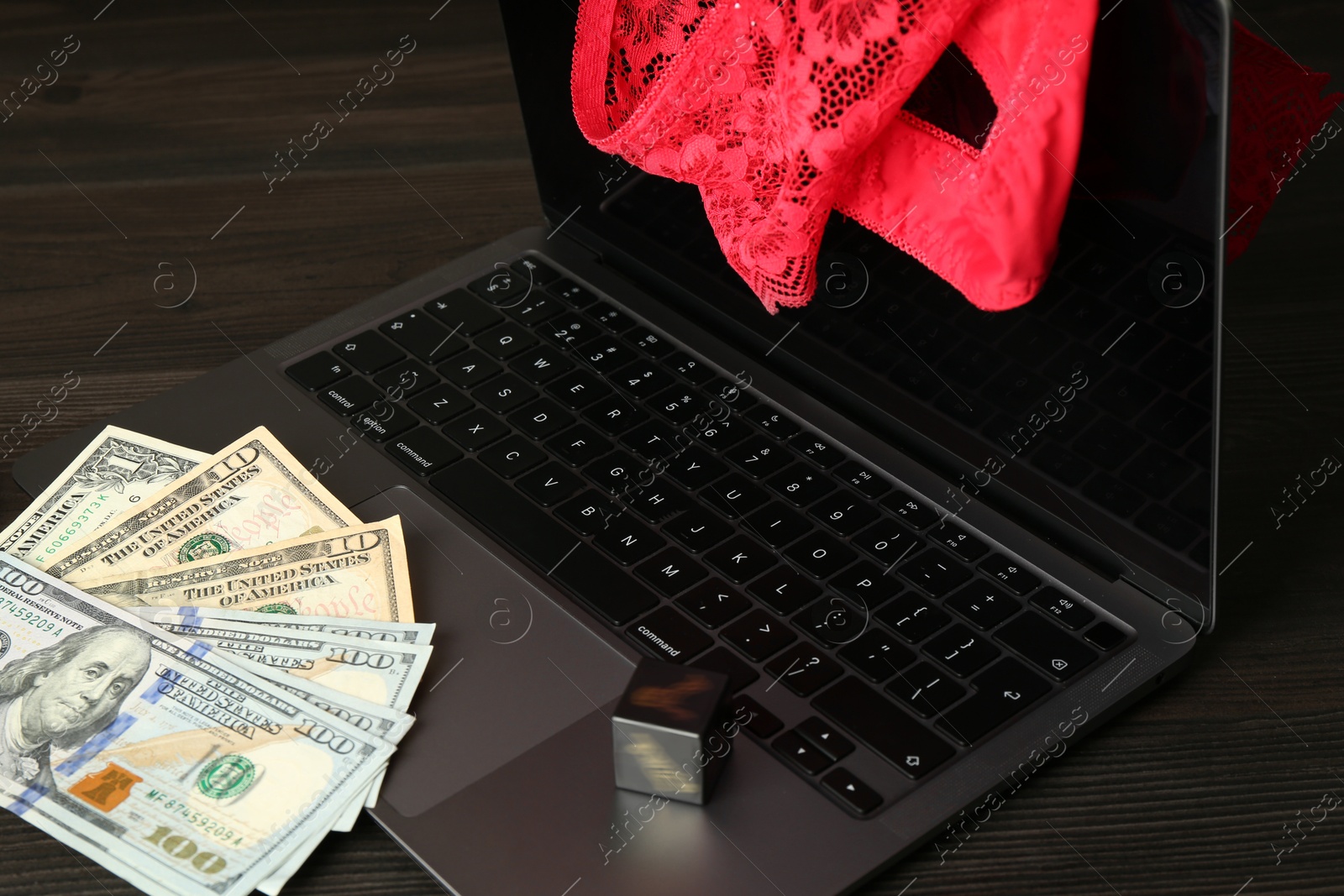 Photo of Sex work. Laptop, lingerie, dice and money on wooden surface, closeup