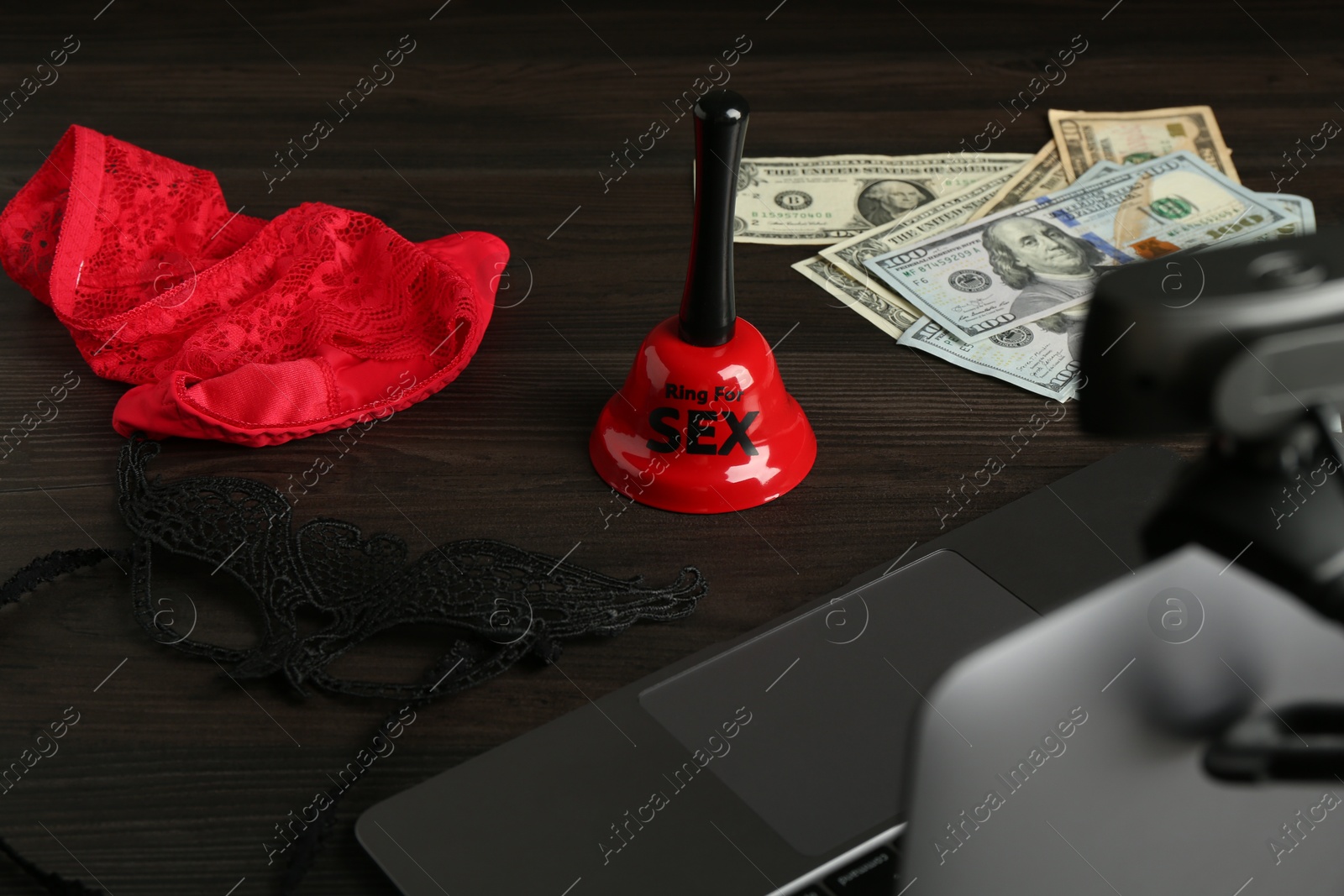 Photo of Sex work. Laptop with web camera. bell, mask, underwear and money on wooden surface, selective focus