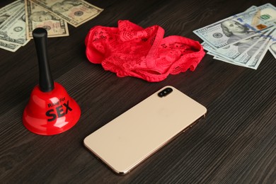 Sex work. Smartphone, bell, underwear and money on wooden surface