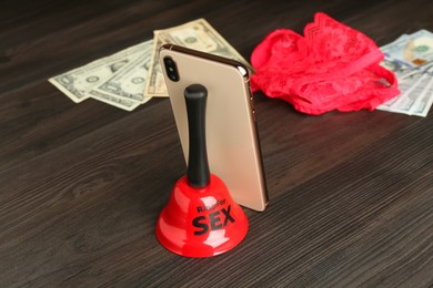 Sex work. Smartphone, bell, underwear and money on wooden surface