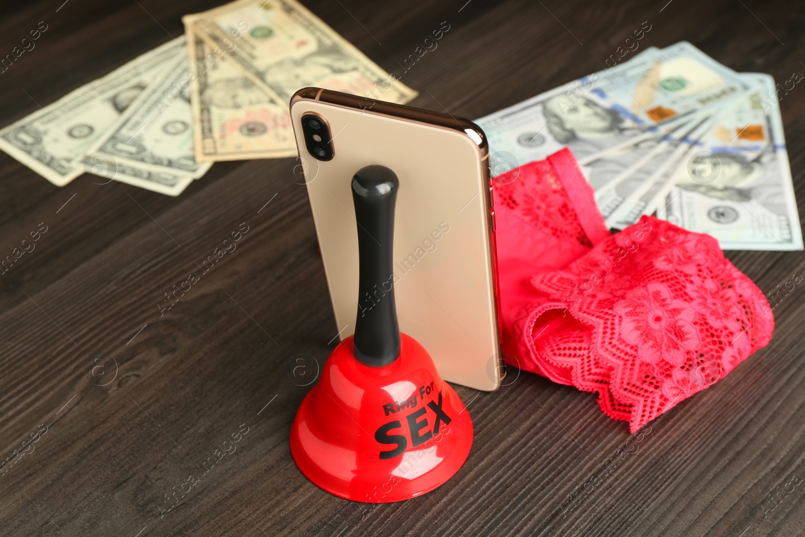 Photo of Sex work. Smartphone, bell, underwear and money on wooden surface