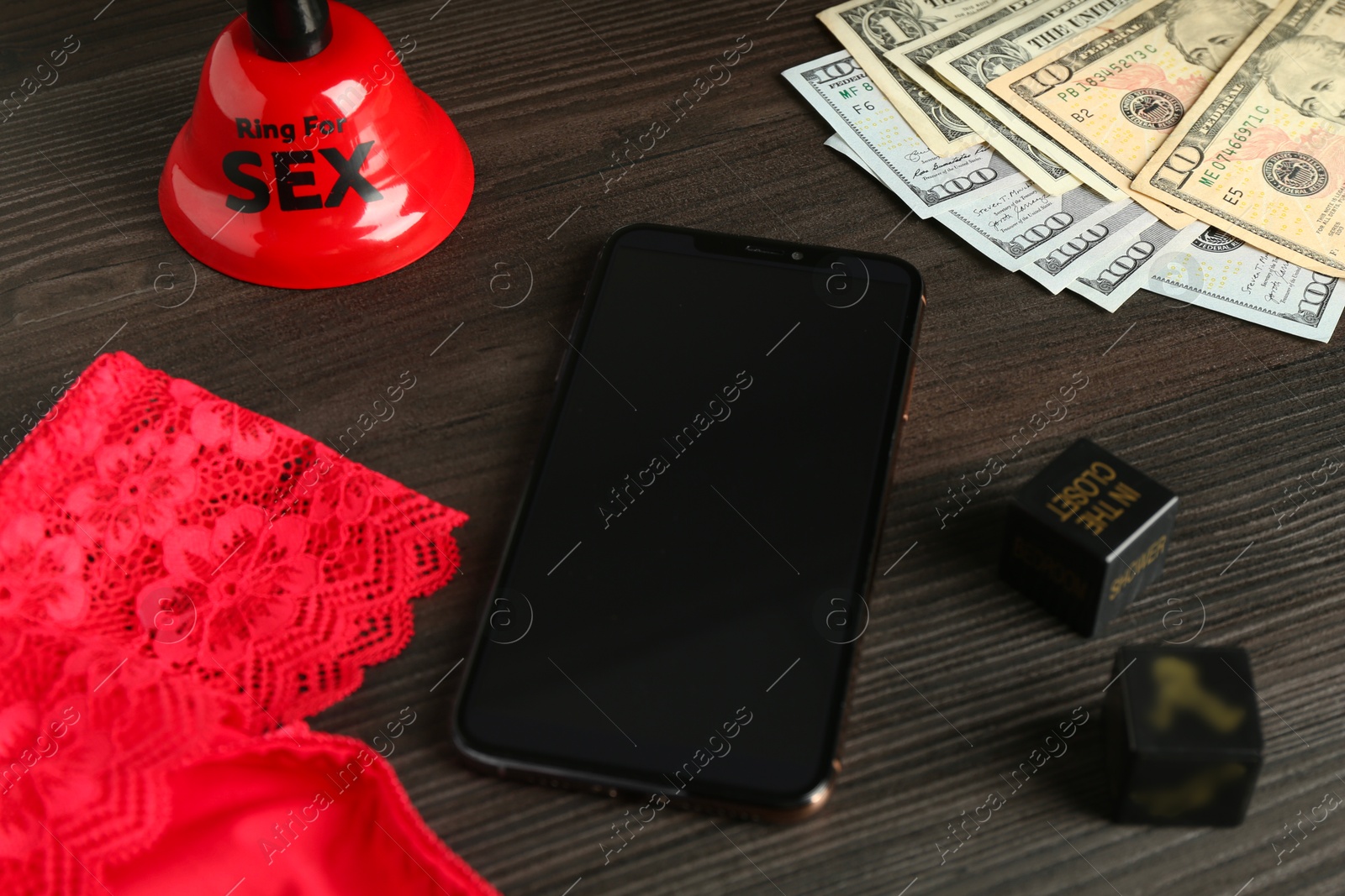 Photo of Sex work. Smartphone, underwear, bell, dice and money on wooden surface, closeup