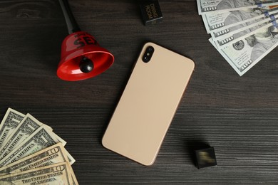 Photo of Sex work. Smartphone, bell, dice and money on wooden surface, flat lay