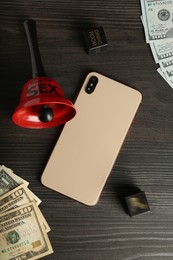 Photo of Sex work. Smartphone, bell, dice and money on wooden surface, flat lay