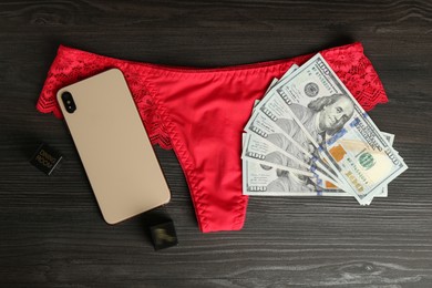 Photo of Sex work. Smartphone, underwear, dice and money on wooden surface, flat lay