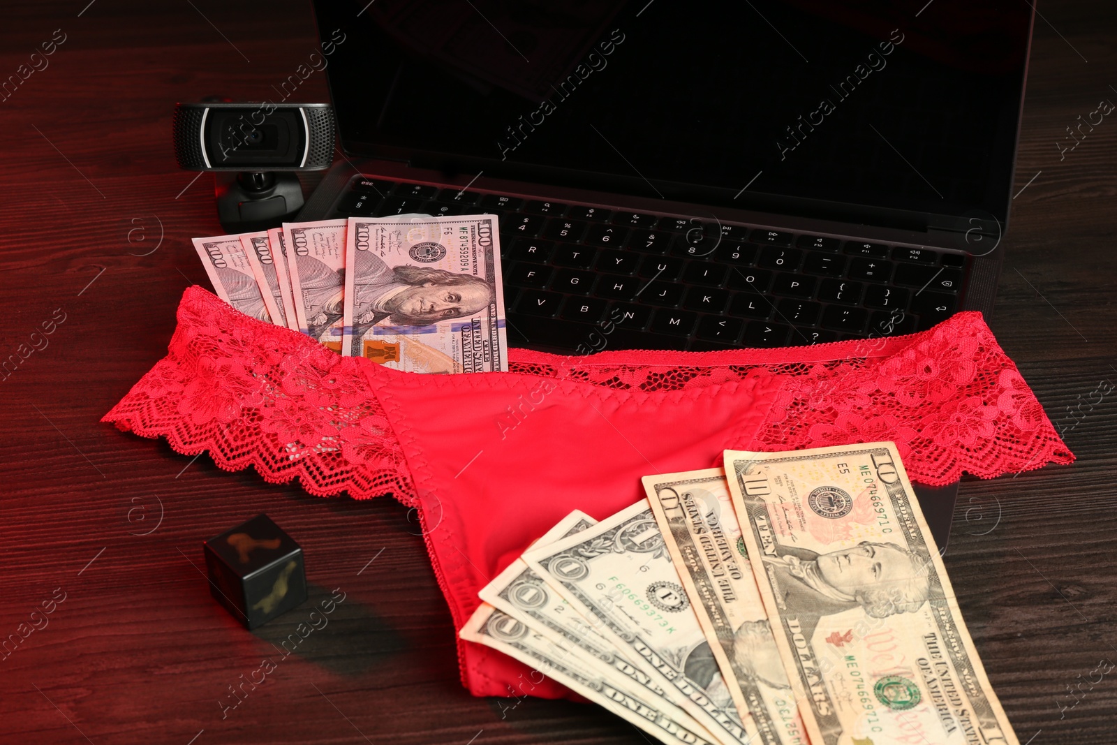 Photo of Sex work. Laptop with panties, dice, web camera and money on wooden surface