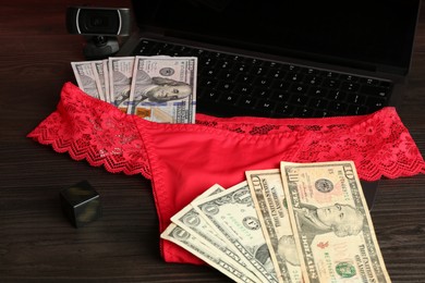 Photo of Sex work. Laptop with panties, dice, web camera and money on wooden surface