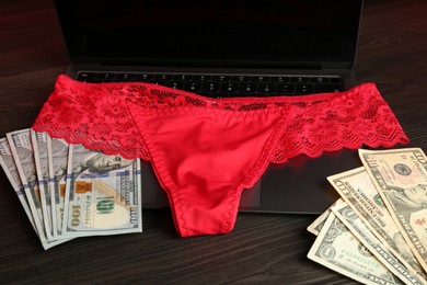 Photo of Sex work. Laptop with panties and money on wooden surface