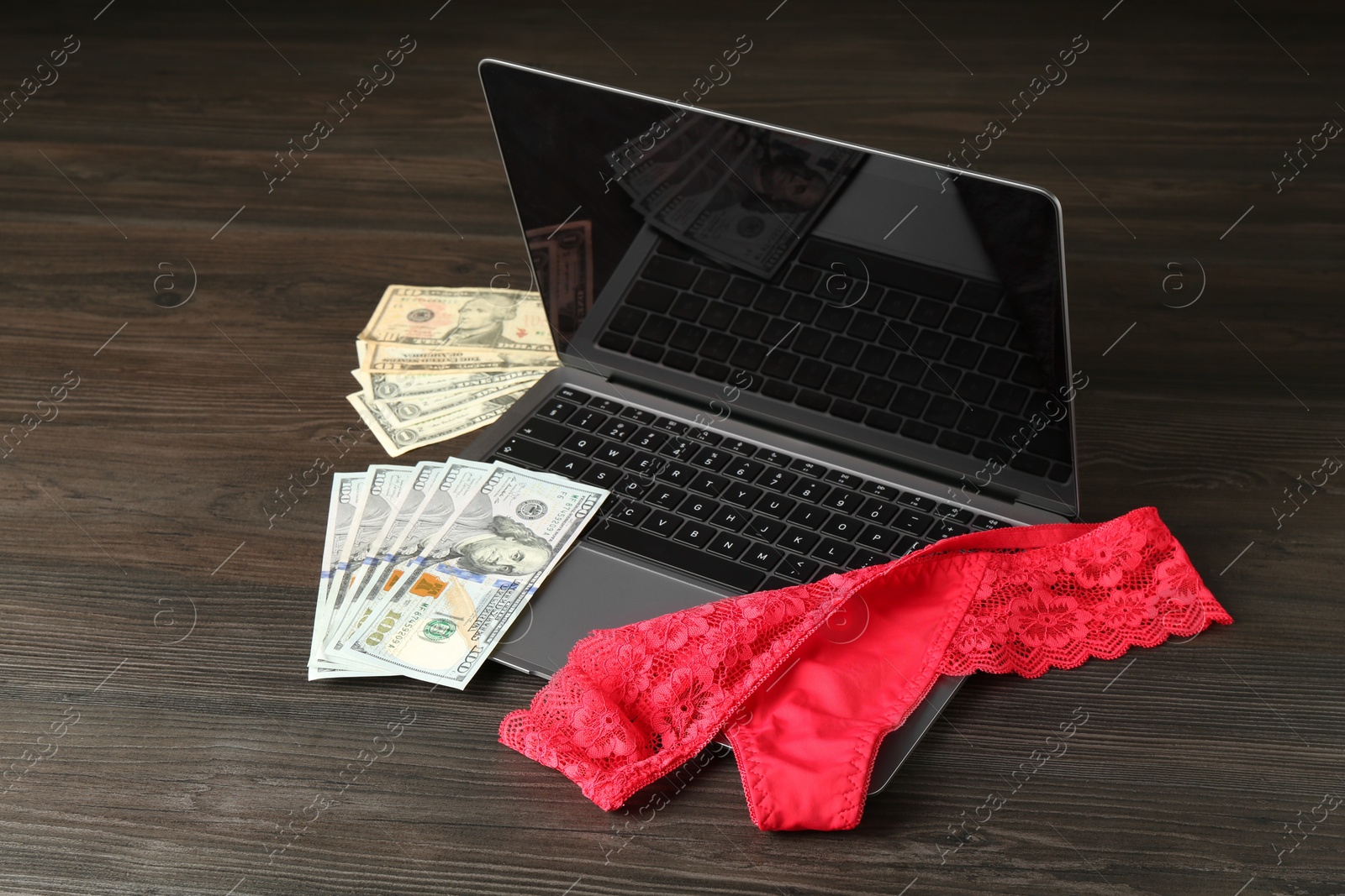 Photo of Sex work. Laptop with panties and money on wooden surface