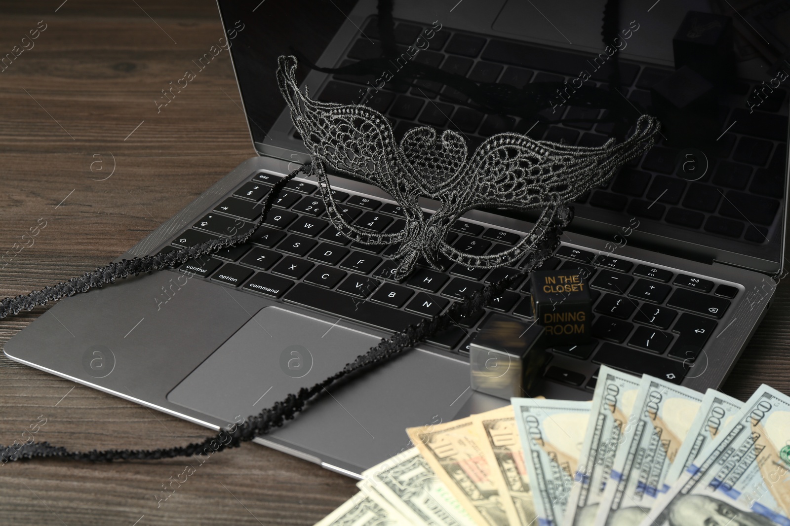 Photo of Sex work. Laptop with mask and money on wooden surface, closeup