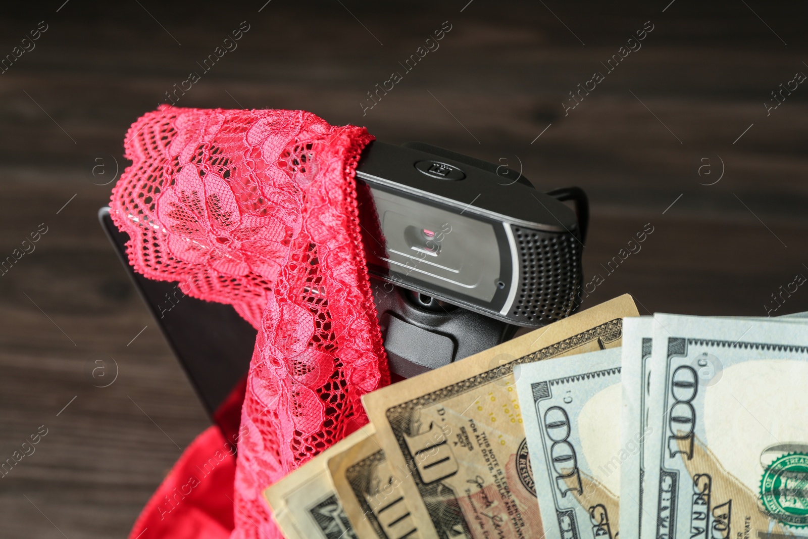 Photo of Sex work. Laptop with web camera, panties and money on wooden surface, closeup