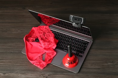 Photo of Sex work. Laptop with web camera, panties and bell on wooden surface