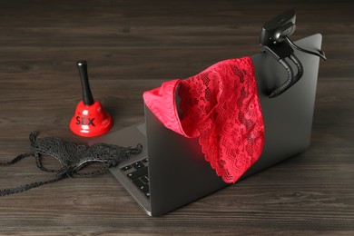 Photo of Sex work. Laptop with web camera, panties, mask and bell on wooden surface