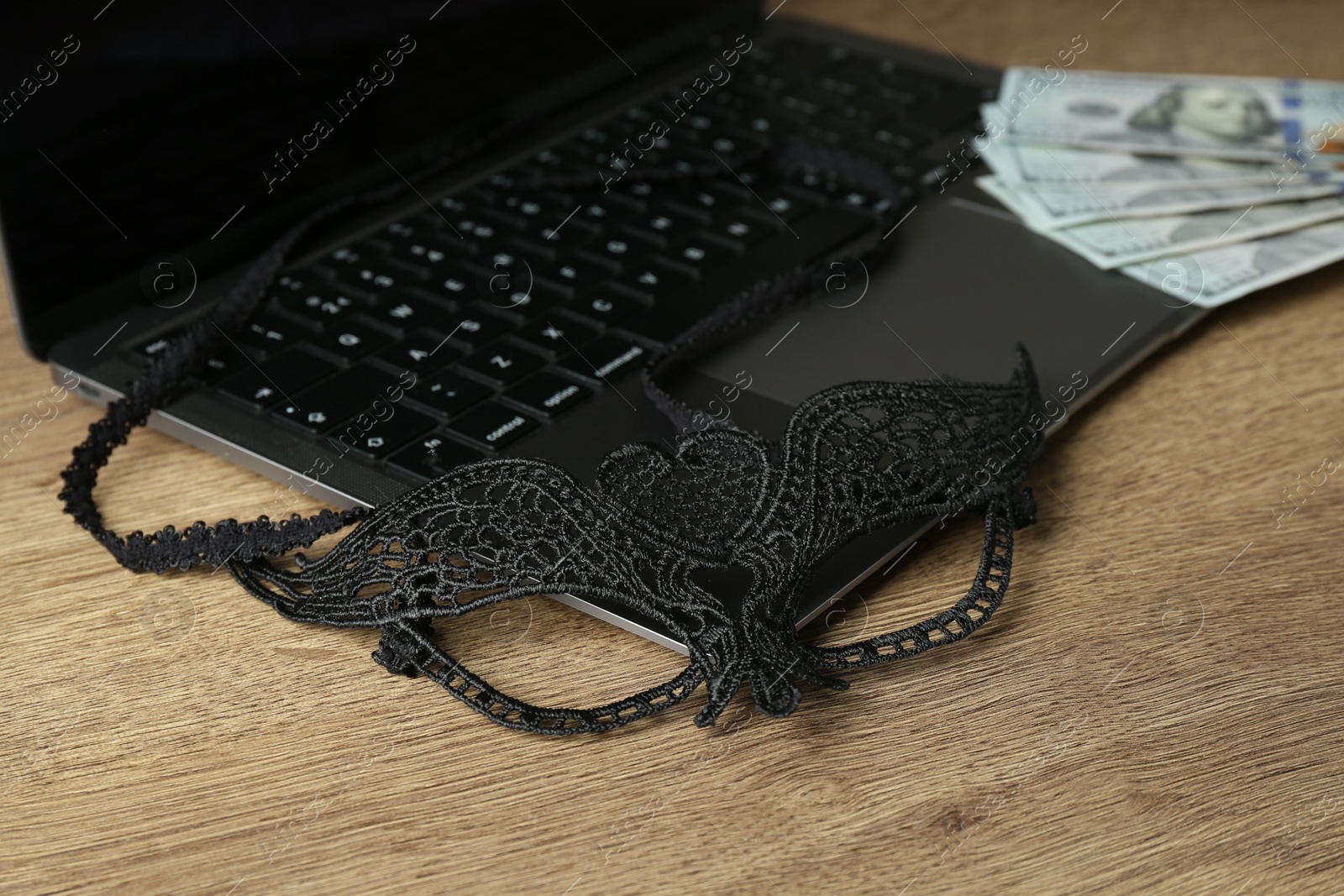 Photo of Sex work. Laptop with mask and money on wooden surface