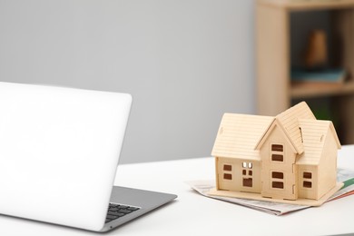 Photo of House hunting. Papers, laptop and house figure on white table