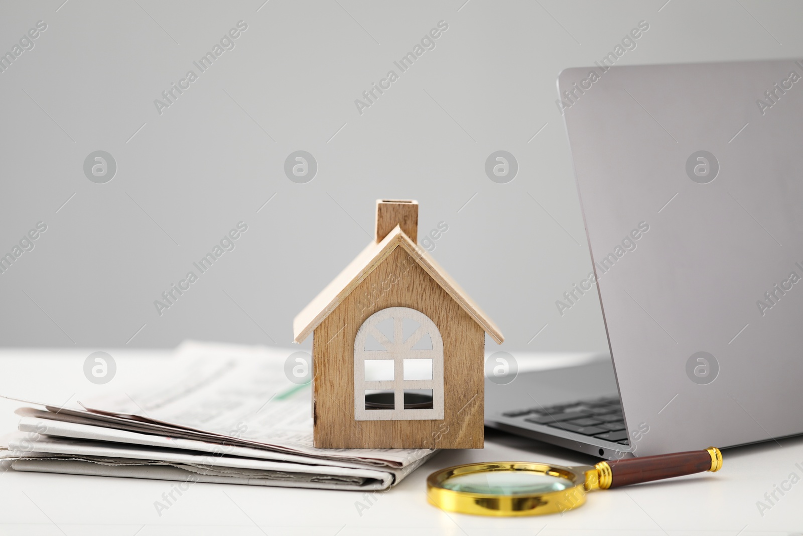 Photo of House hunting. Papers, laptop, magnifying glass and house figure on white table