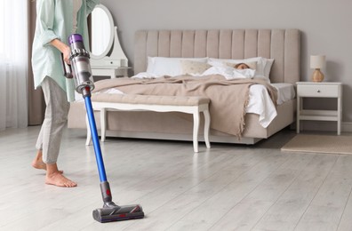 Photo of Young woman cleaning floor with cordless vacuum cleaner while her daughter sleeping in bedroom, closeup