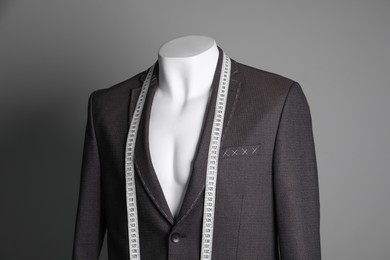 Photo of Semi-ready jacket with tailor's measuring tape on mannequin against grey background