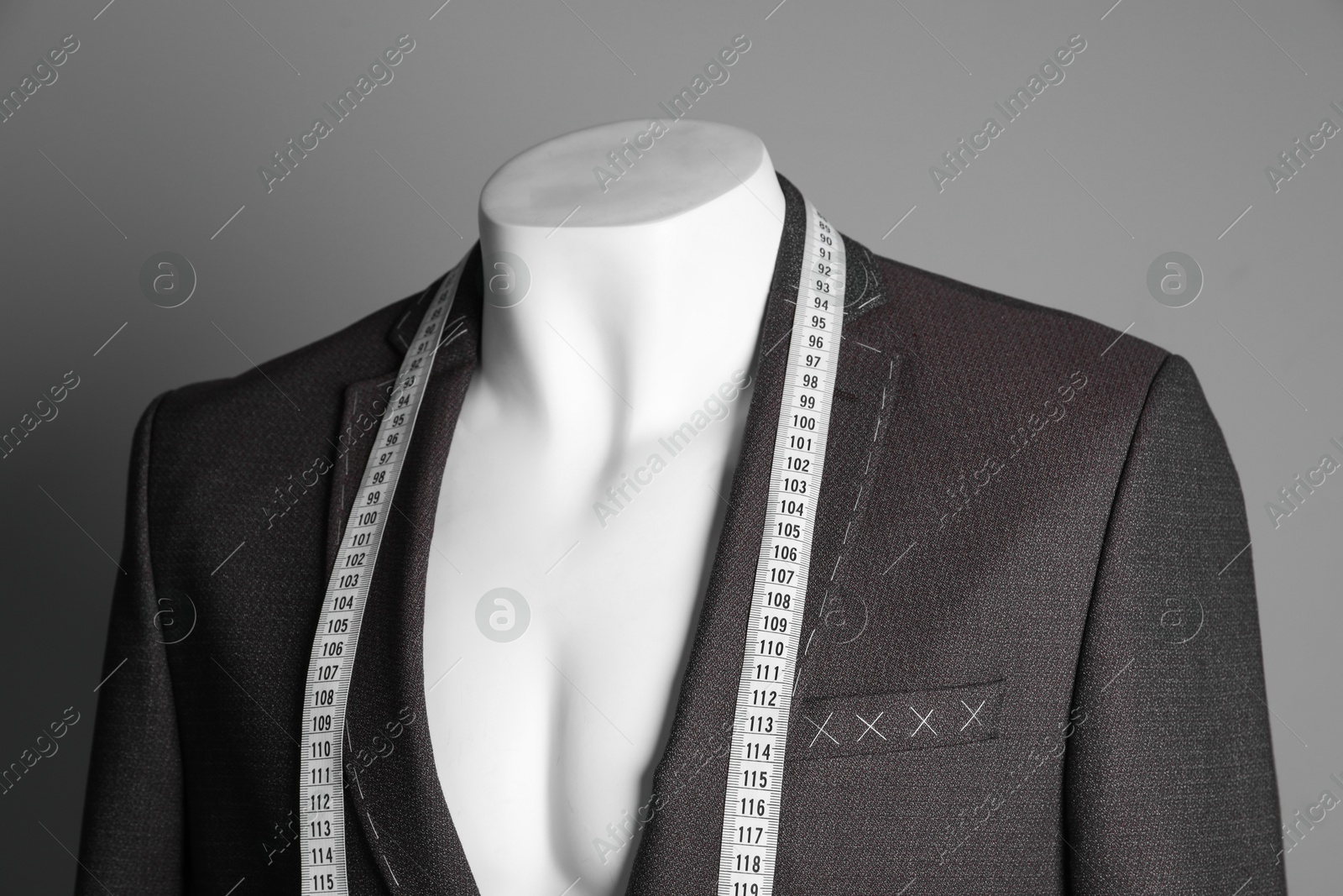 Photo of Semi-ready jacket with tailor's measuring tape on mannequin against grey background, closeup