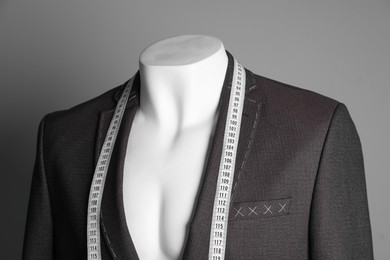 Photo of Semi-ready jacket with tailor's measuring tape on mannequin against grey background, closeup