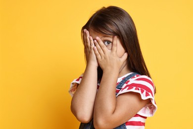 Photo of Scared little girl covering face with hands on orange background. Space for text