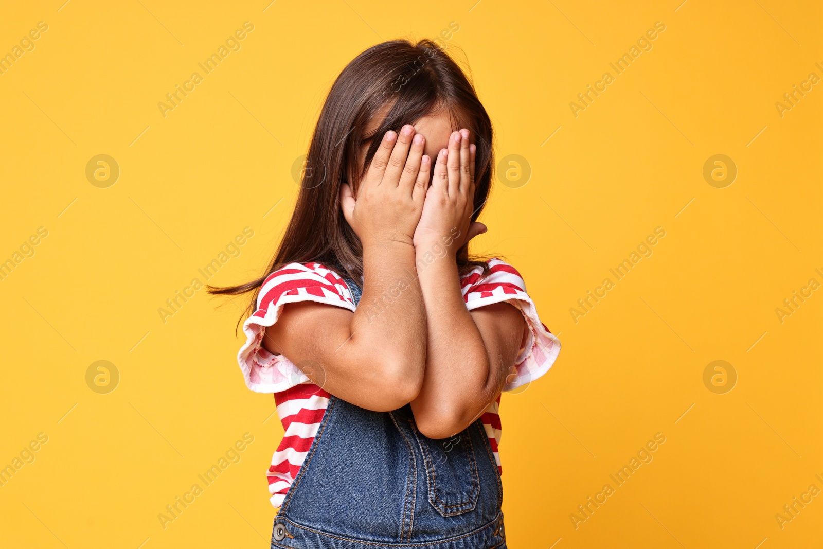 Photo of Scared little girl covering face with hands on orange background