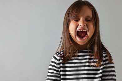 Photo of Scared little girl screaming on grey background. Space for text