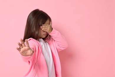 Photo of Scared little girl covering face with hands on pink background. Space for text